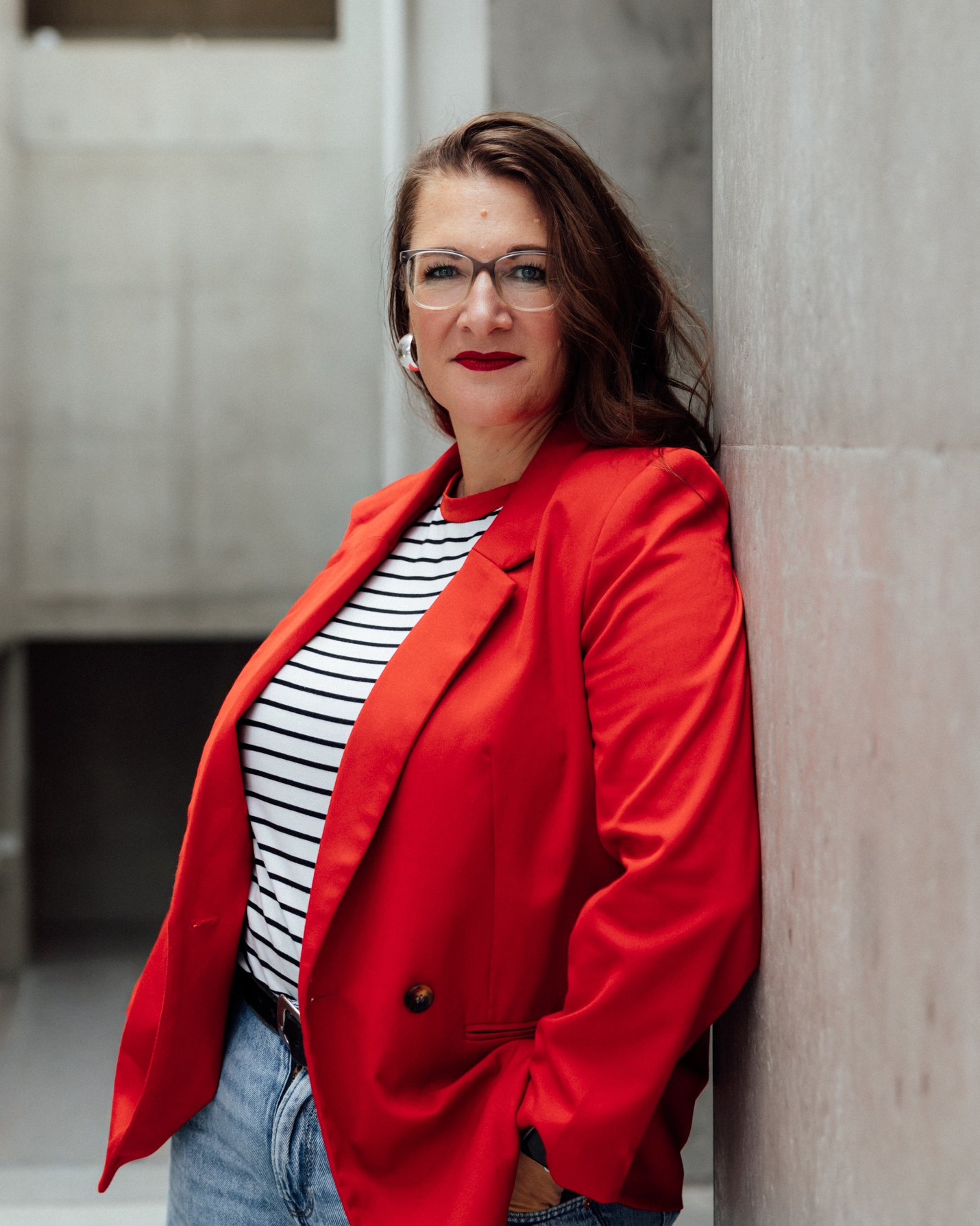 Ines Schäfer, SEELENfotogräfin®, im roten Blazer an einer Betonwand – Personal Branding Fotografin aus Tönisvorst